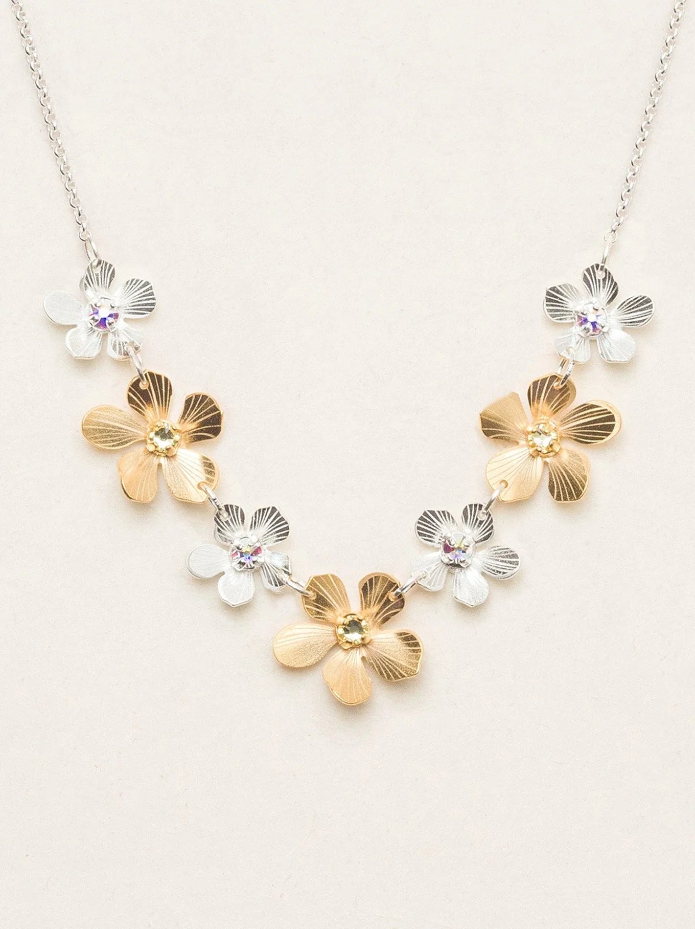 This necklace features 18k gold plated, and silver plated Plumeria flowers, each accented with a sparkling crystal stone. Materials: 18k gold plated flowers. Silver plated flowers and chain. Crystal. Dimensions: Adjustable chain - 18-20". Gold flowers: 0.5" x 0.5". Silver flowers: 0.35" x 0.35".