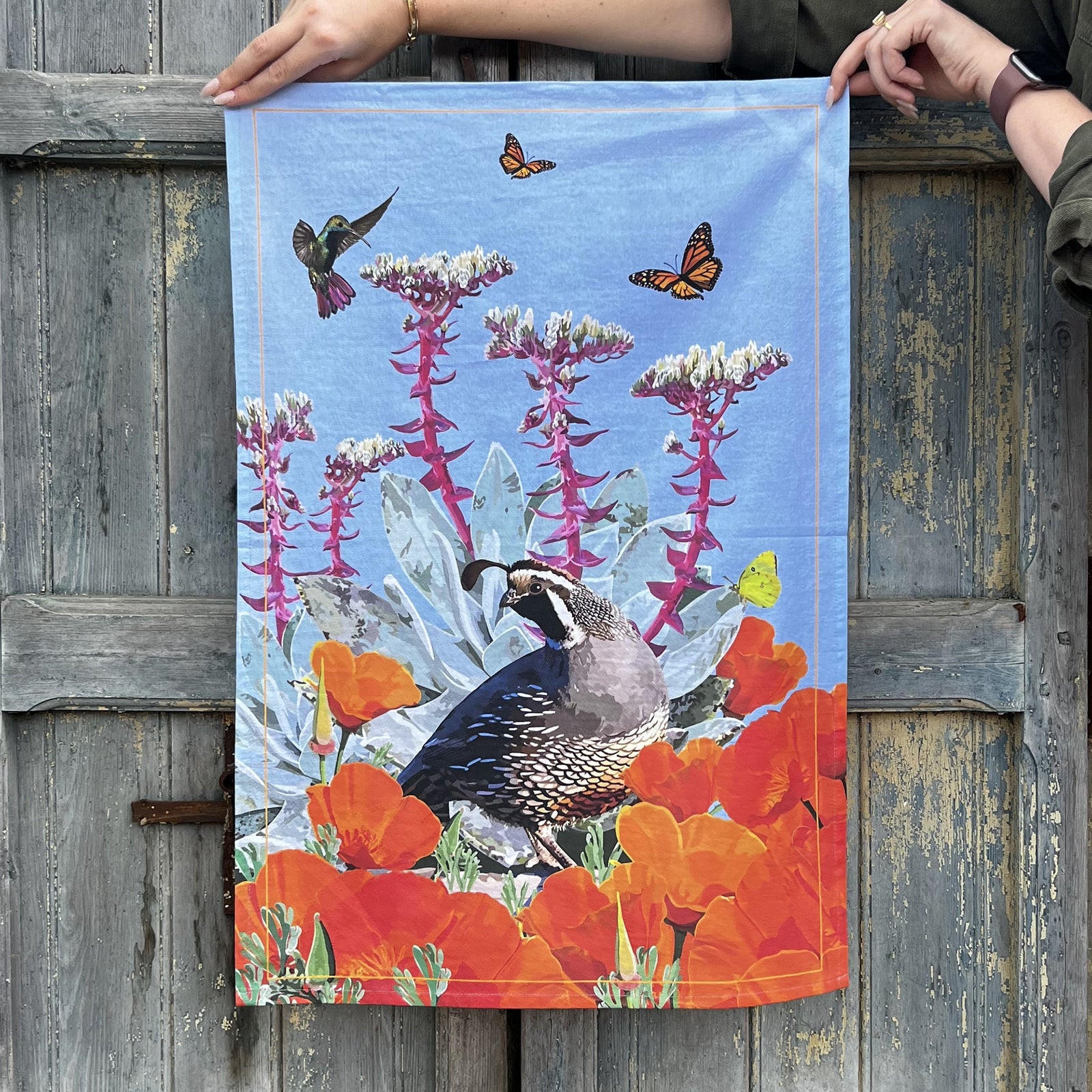 Tea towel with an Illustration of a California Quail among flowers and butterflies on a blue background