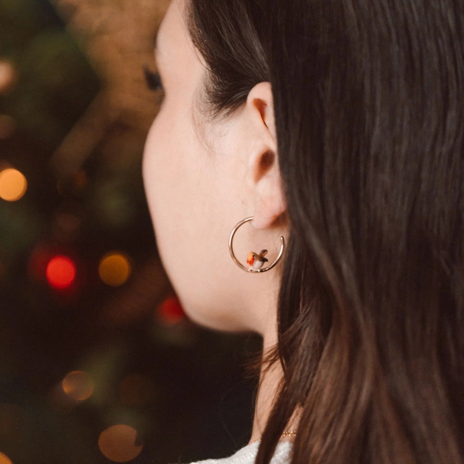 Gold hoop earrings with a small enamel robin at the bottom of the hoop, on a white background.