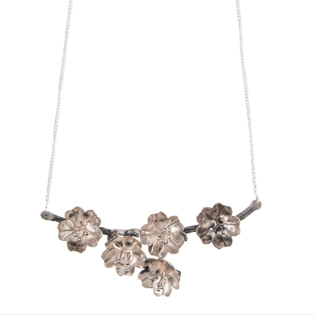 Indulge in the dramatic beauty inspired by Hokusai’s small blossoms with this handcrafted sterling silver cherry blossom branch necklace. Meticulously shaped and textured, it captures the essence of cherry blossoms on a branch, offering a dramatic and unique piece of wearable art. Material: Sterling silver Dimensions: Branch/blossoms: 4" x 1.5". Chain length 15"