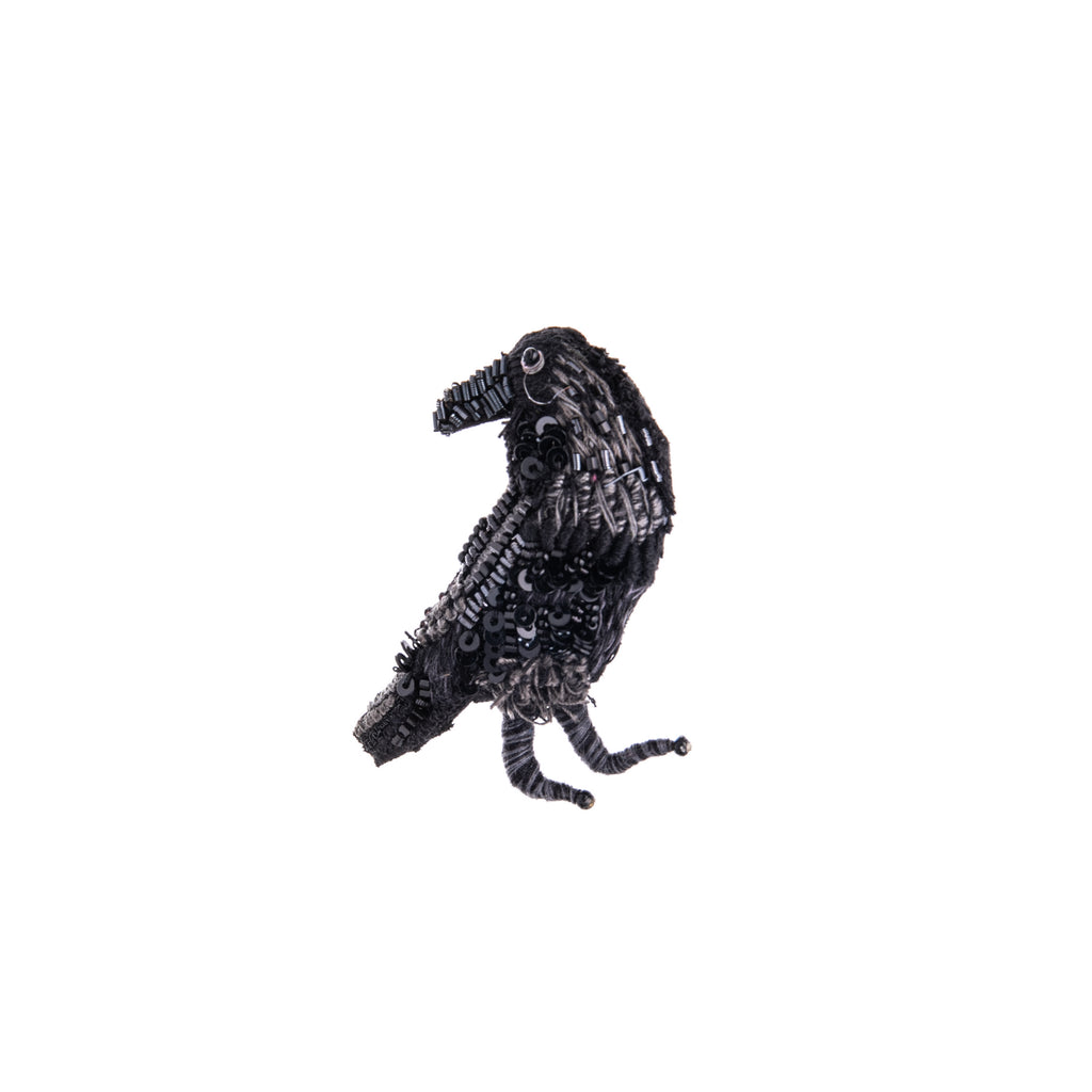 This beautifully detailed, hand-made raven brooch features intricate beading and embroidery on a base of cotton and felt. Add this pin to your outfit for a dose of spooky, or just to show your love of this charming corvid. Hand-made Materials: Cotton, felt, metal, beads Dimensions: 2" x 2"