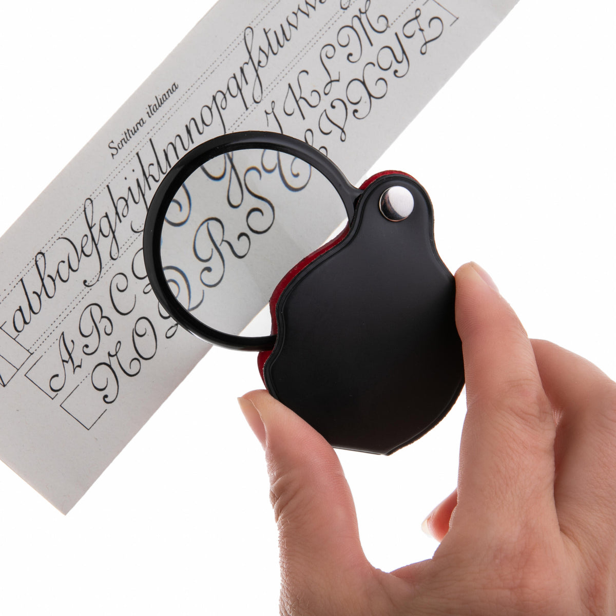 Hand holding a magnifying glass over printed calligraphy on a white background