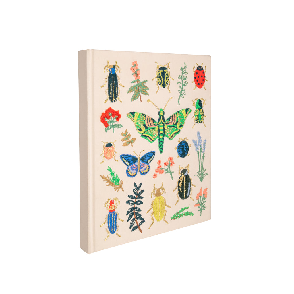 This embroidered sketchbook is a large, hardcover journal with 108 unlined pages of thick paper perfect for sketching, drawing, and journaling. The cover is wrapped in cream book cloth and embroidered with beetles and bugs with metallic gold accents. Attached grosgrain ribbon bookmark. 10.25" L × 8.25".