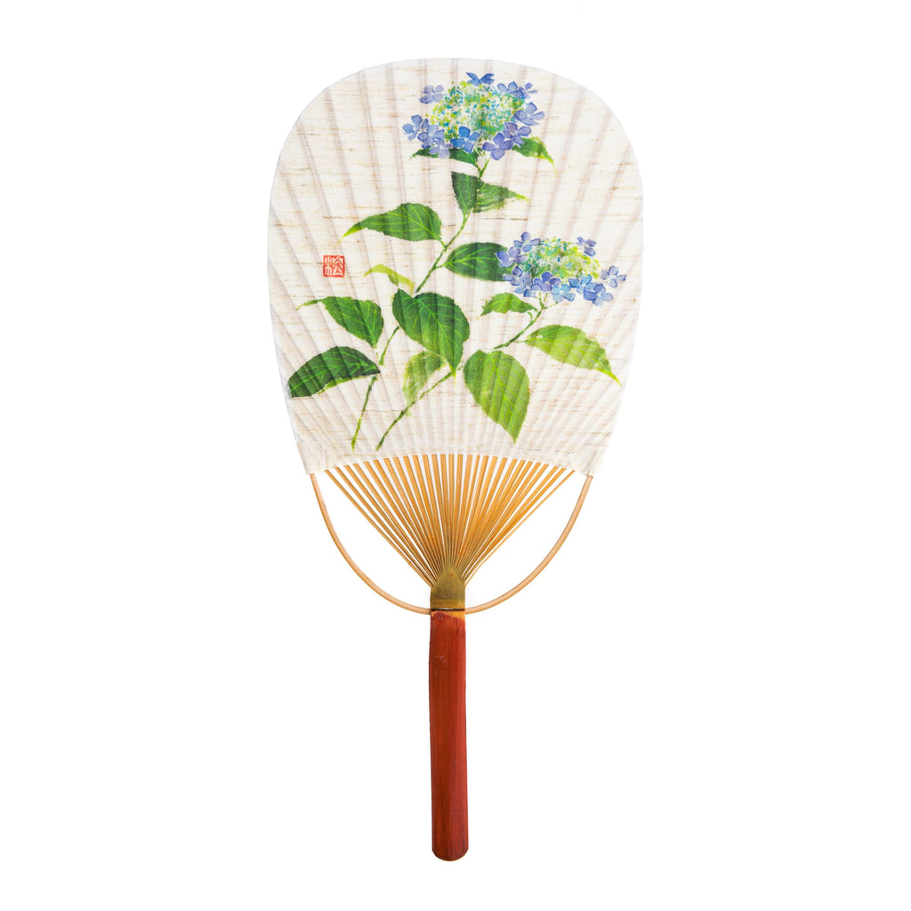 The uchiwa fan is an indispensable item during Japanese summer. These beautifully constructed and decorated fans are traditionally used for both fanning and also for repelling mosquitos and flies. This design features a bamboo handle and frame decorated with a beautiful hydrangea print. Bamboo, paper. 14.5" x 7".