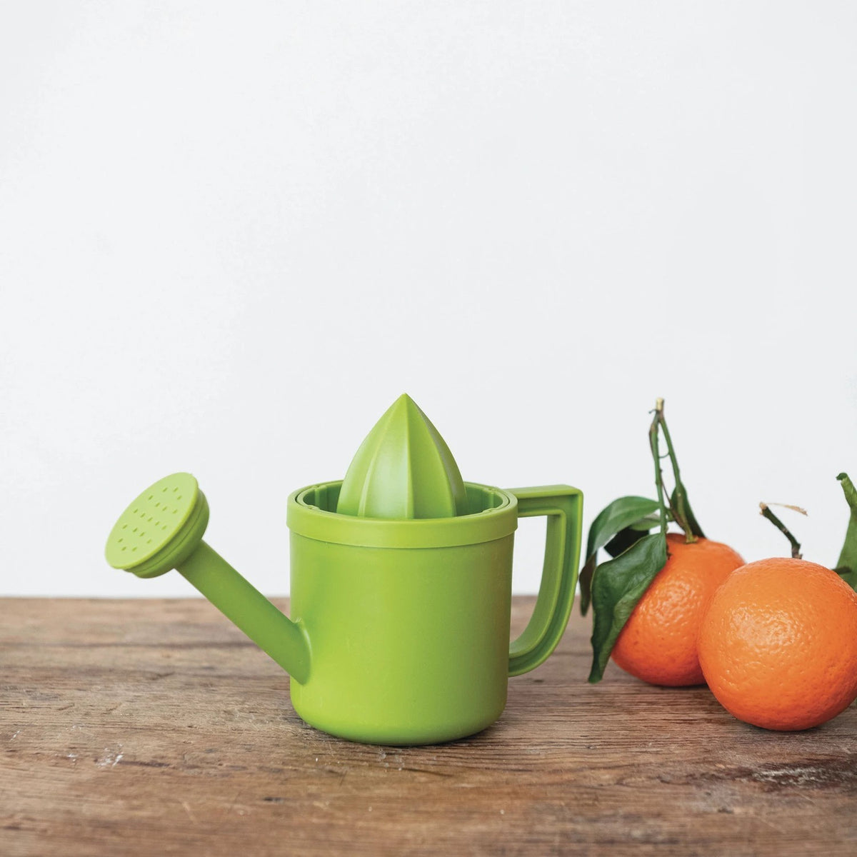 Green citrus juicer, shaped like a watering can with oranges on a wooden surface