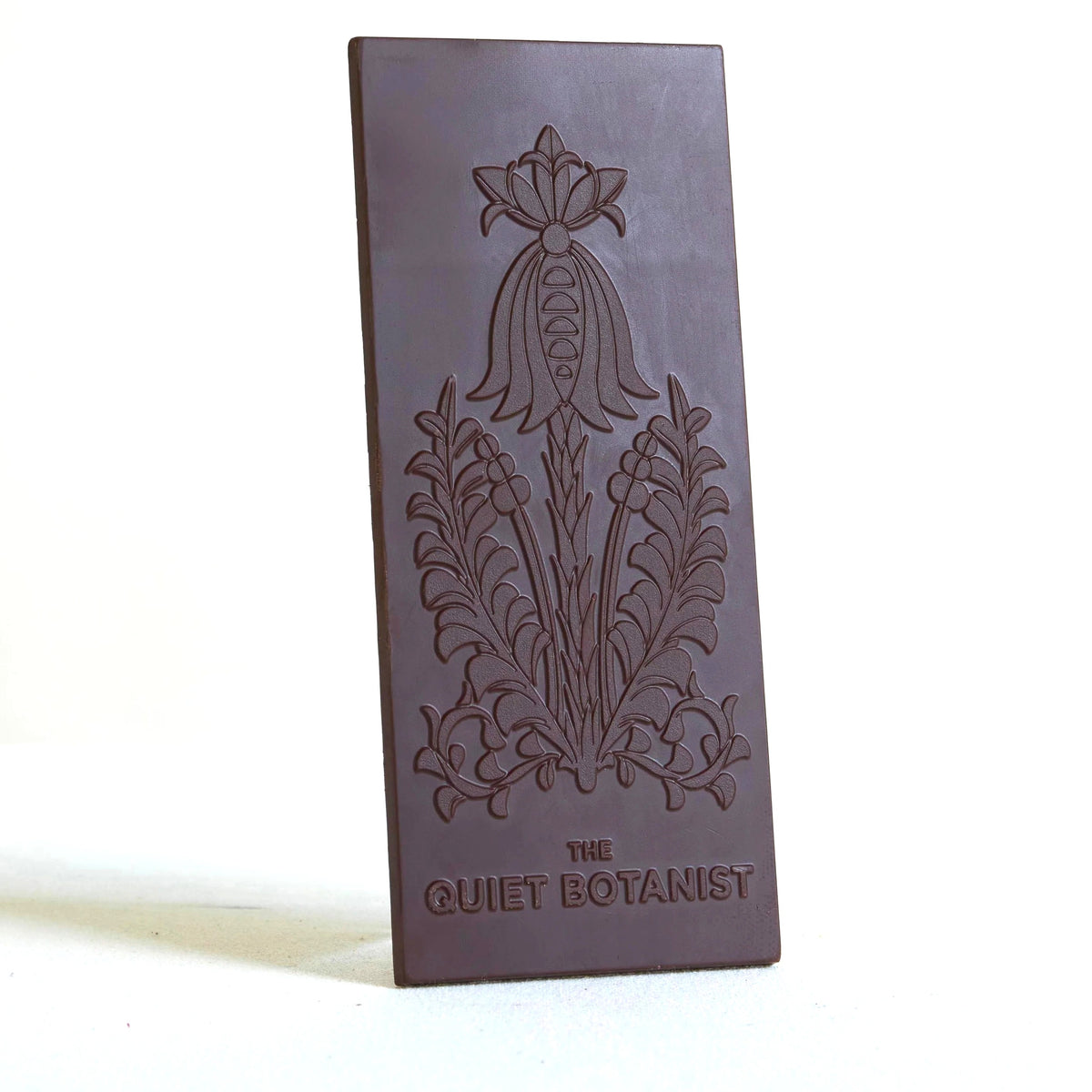 Dark chocolate bar with floral embossing and 'The Quiet Botanist' text on a white background