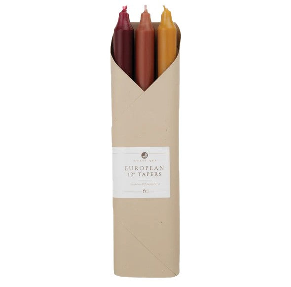 Set of six candles in red, brown, and yellow in a cardboard holder with a label on a white background.
