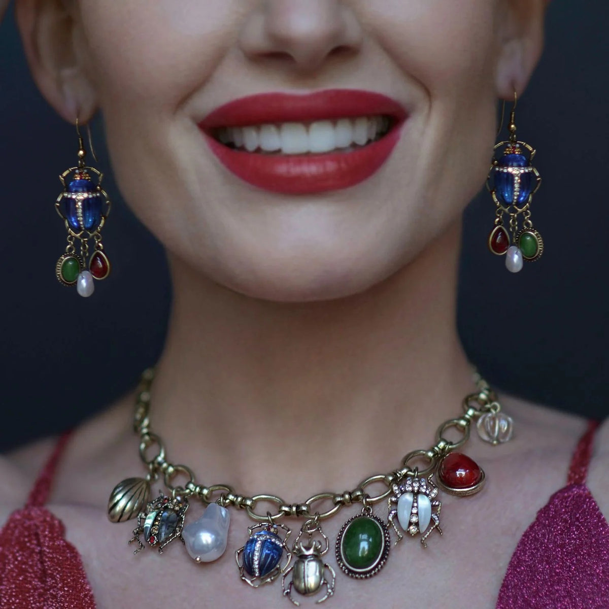 Close-up of a woman wearing a colorful bug-charm necklace and earrings with a blurred background