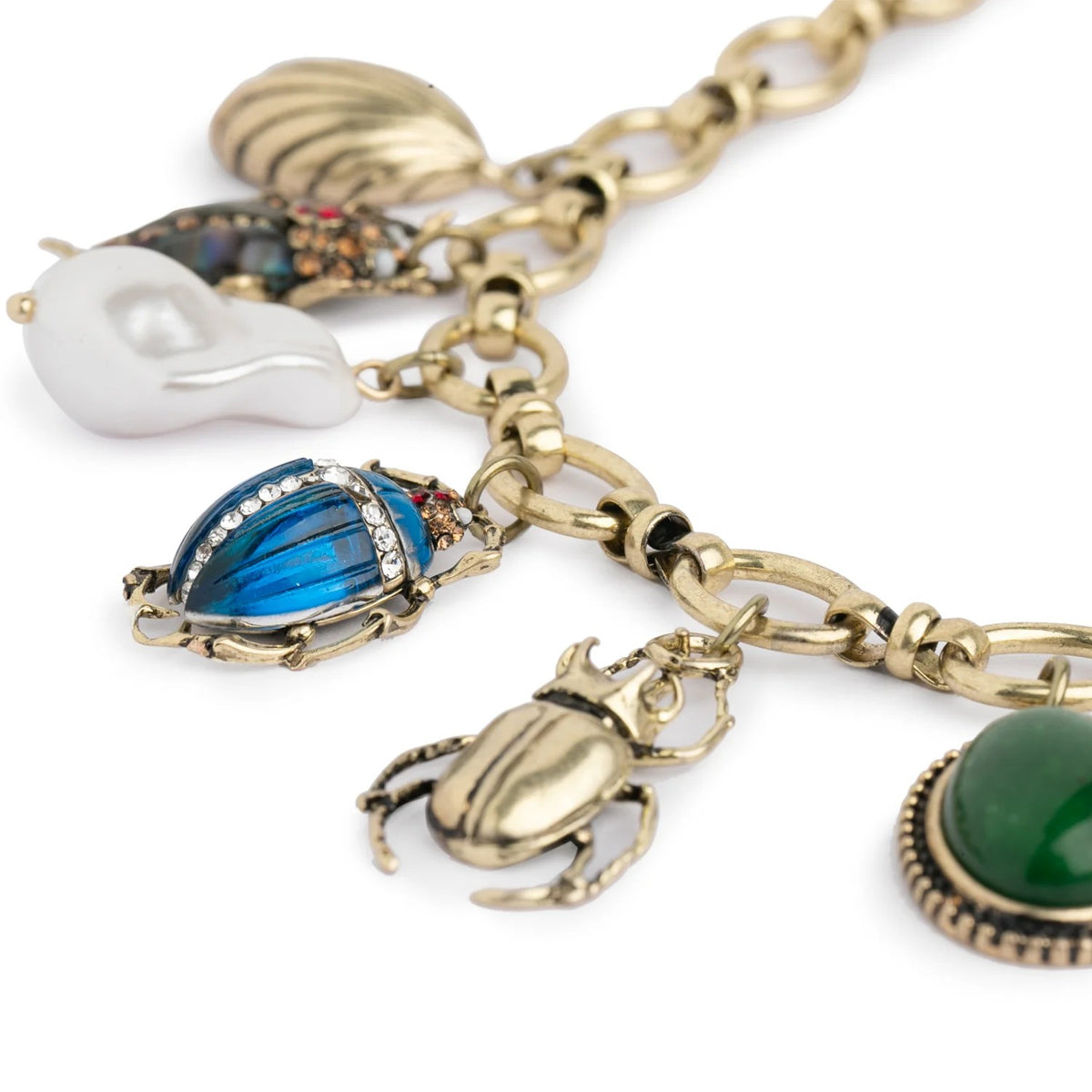 Gold charm necklace with various charms including a blue beetle, green stone, and white shell on a white background.