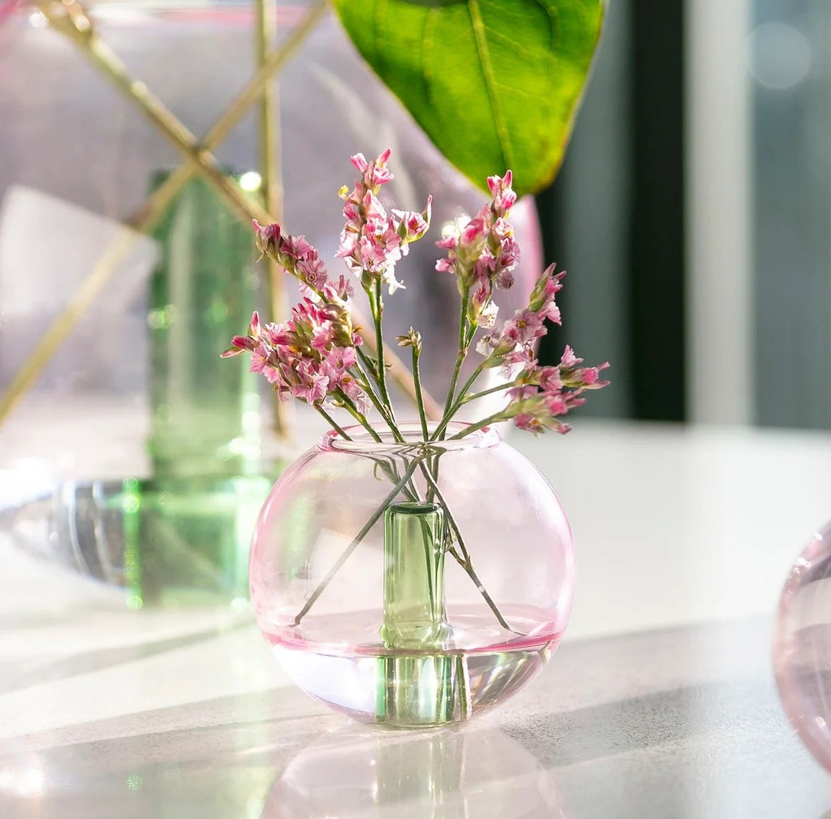 Clear glass vase with pink flowers on a reflective surface