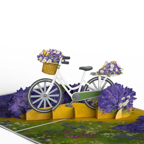 This delightful pop-up greeting card sends out the joyous vibes of a spring day. The card depicts a white bicycle filled with baskets and bunches of daisies and lavender. In addition to the pop-up card, a blank notecard featuring a hand-tied lavender bouquet is included, so that you have plenty of space for your special message. Pop-up greeting card with additional note card and envelope Card size: 7" x 5"