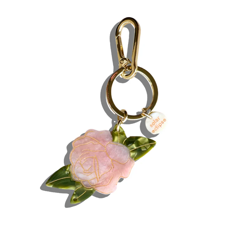 This pretty pink keychain/bag charm will add a pop of rosy radiance to your purse, backpack, keys, and more. This adorable accessory is crafted from a biodegradable acetate made from wood pulp. It is finished off with a sturdy metal keyring and a carabiner clip.