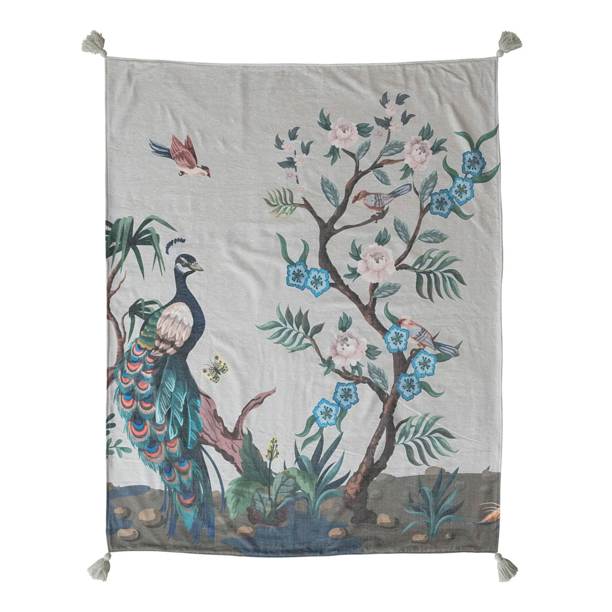 A square woven textile hanging or tapestry with tassels at the corners, featuring a printed peacock, flowering tree, birds, and foliage on a light neutral background.