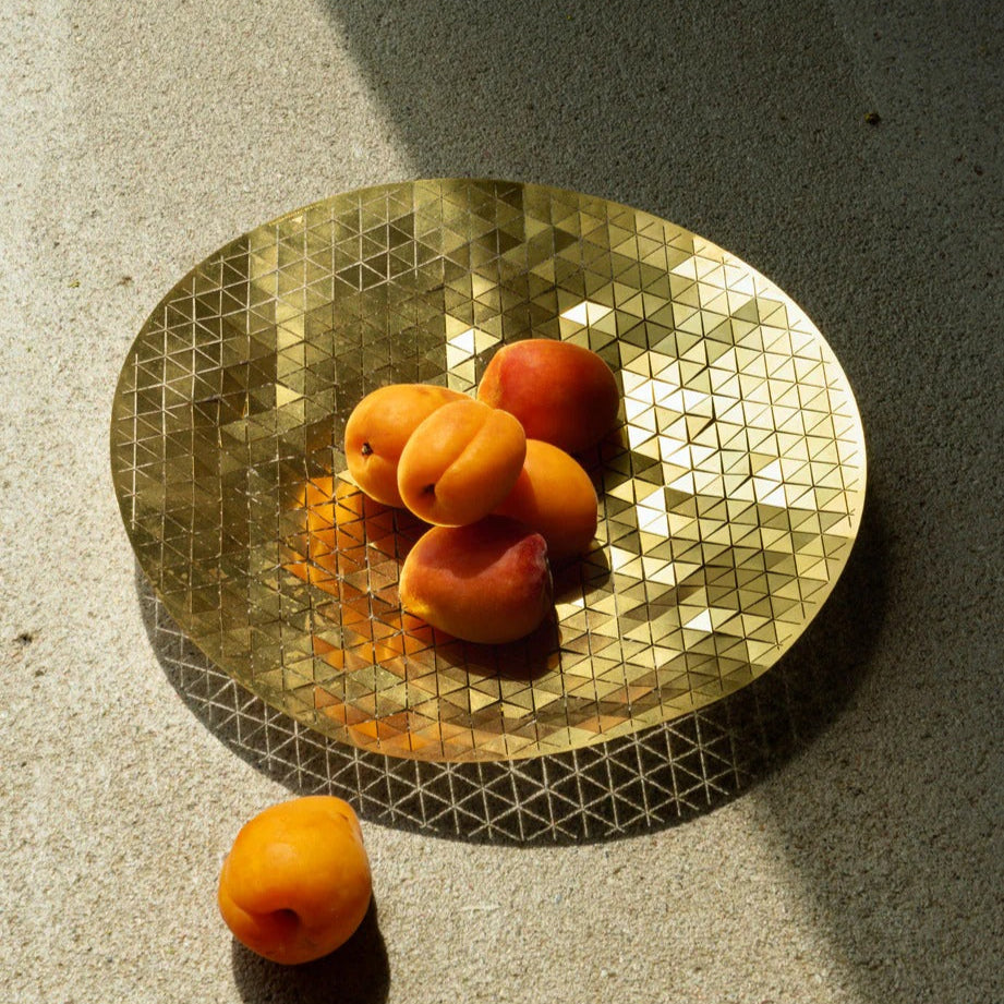 Gold decorative plate with geometric pattern on a concrete surface, containing apricots.
