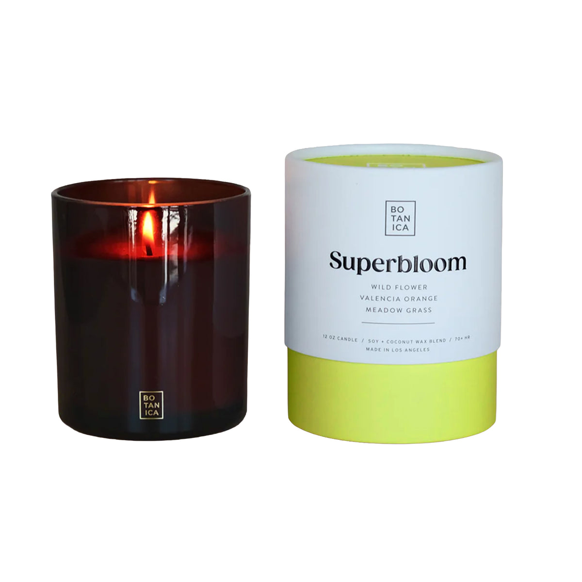 Lit candle in a dark container next to its packaging labeled 'Superbloom' on a white background