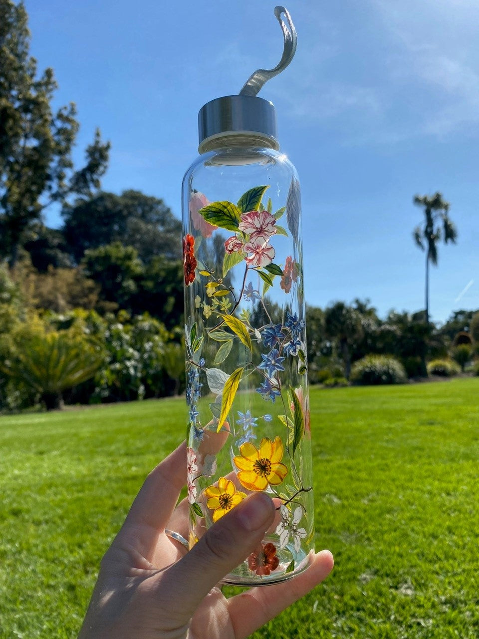 Pretty up your water game with this floral-patterned glass water bottle. Made of heat-resistant, tough borosilicate glass. Perfect for hikes, picnics, and anywhere you might need a little portable hydration. 18.6 oz. Heat-resistant borosilicate glass. Includes stainless steel cap and fabric carrying strap. Handwash.